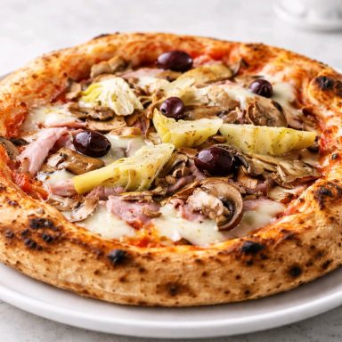 Pizza garnie de champignons, jambon, artichauts et olives noires sur croûte dorée.